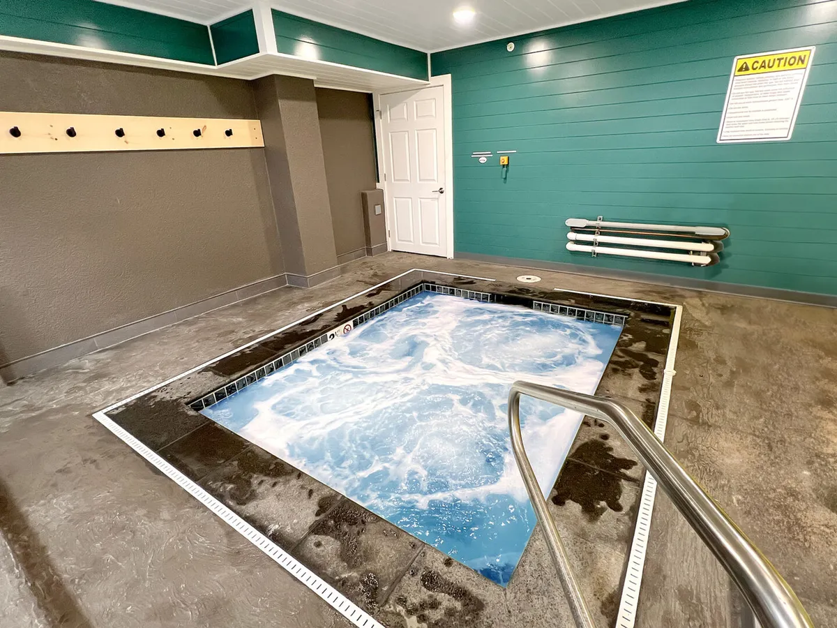 A tranquil indoor hot tub with a handrail, warning sign, and coat hooks along the wall. The space is warm and inviting, ideal for relaxation and socializing after a busy day.