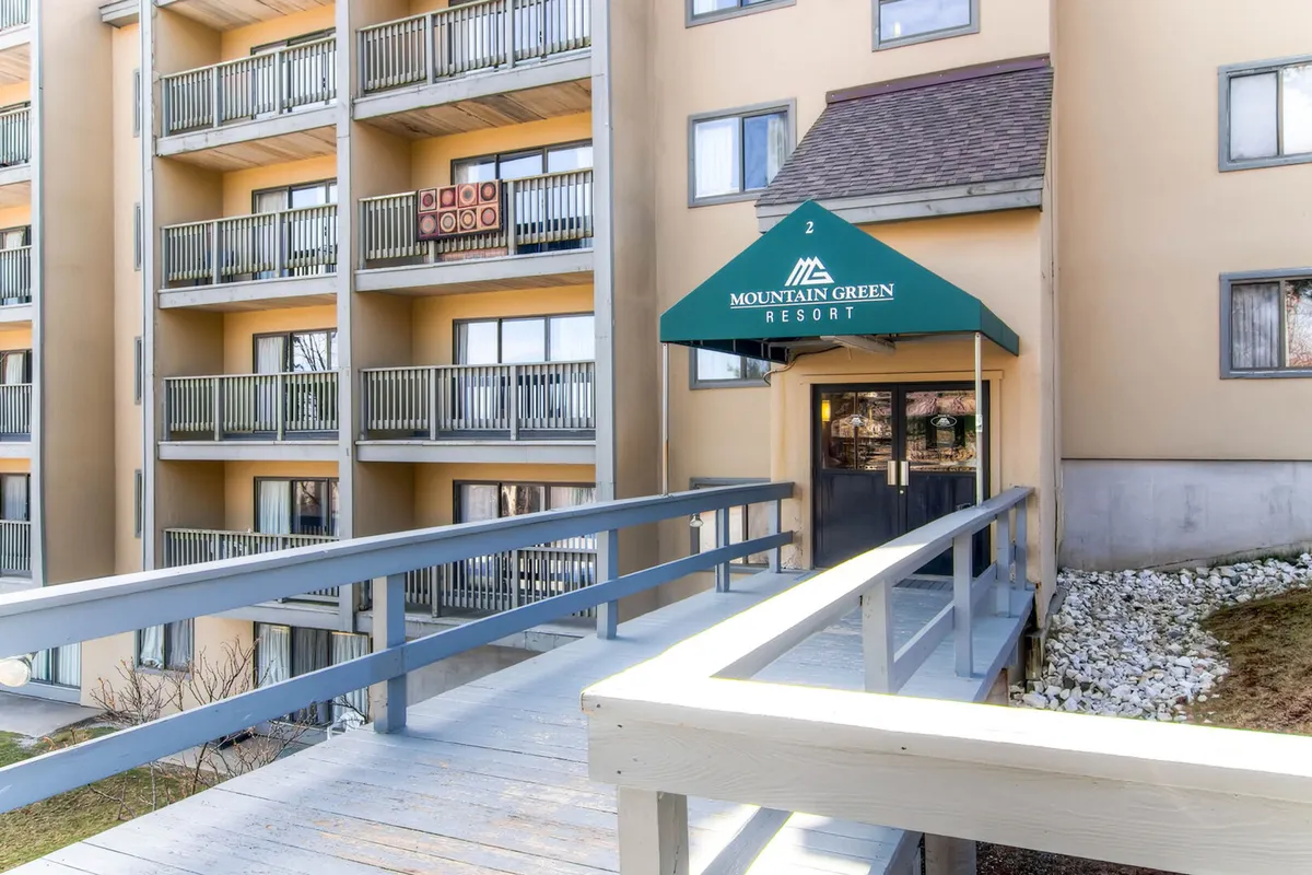 The image showcases the main entrance awning, multi-level balconies, and a welcoming pathway leading into the resort. The scene hints at the arrival experience and the communal spaces where families and groups can gather before heading out to enjoy the amenities.