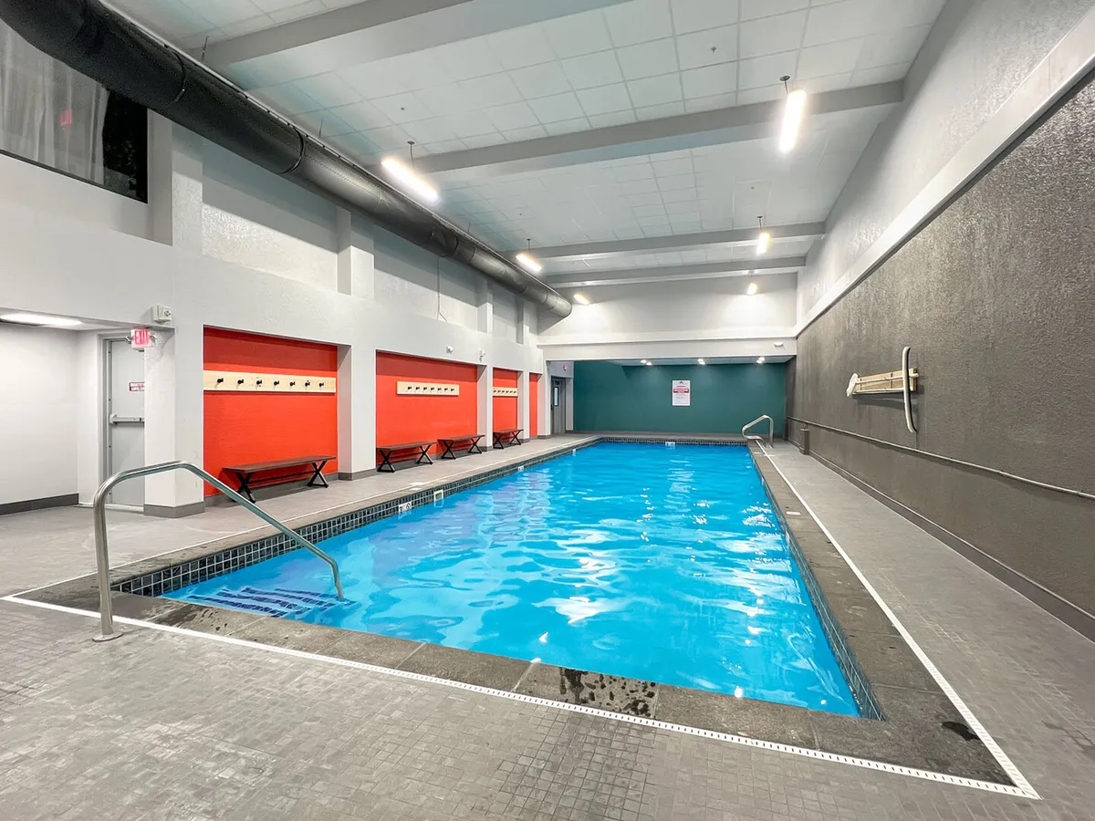 A bright, modern indoor swimming pool area features bold red accents and benches along the wall, creating a lively spot for swimming and socializing, regardless of the weather outside.