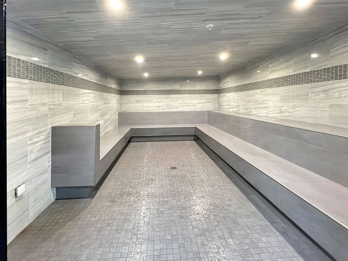 An inviting interior wellness space featuring smooth tiled benches, textured flooring, and soft overhead lighting. The spa-like environment suggests opportunities for relaxation, mindfulness, and social wellness activities, echoing the section’s mention of saunas, steam rooms, and spa treatments.